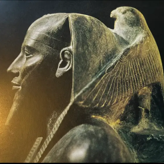 Ancient Egyptian stone statue of a seated figure with a falcon at the shoulder.